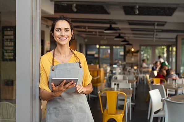 Woman in an apron holding a tablet, outside of a storefront.